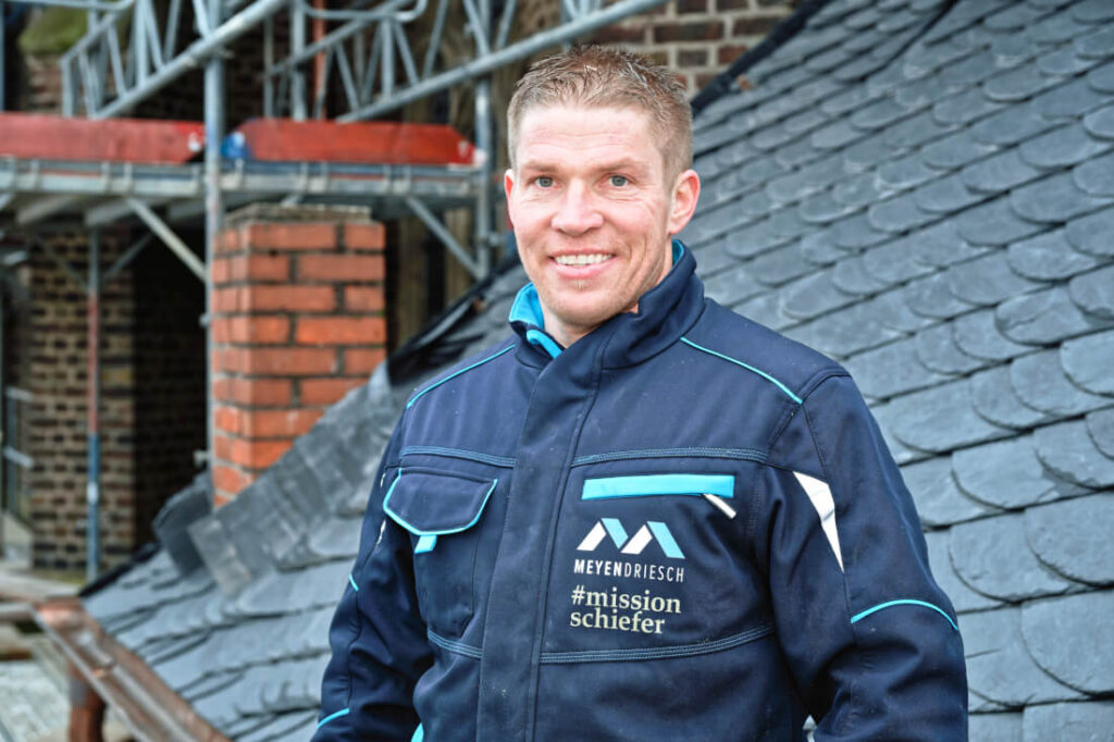 Portrait von Bastian Meyendriesch, Geschäftsführer von Meyendriesch-Dach, auf einer Baustelle vor frisch eingedecktem Schieferdach – #missionschiefer, Hunsrück