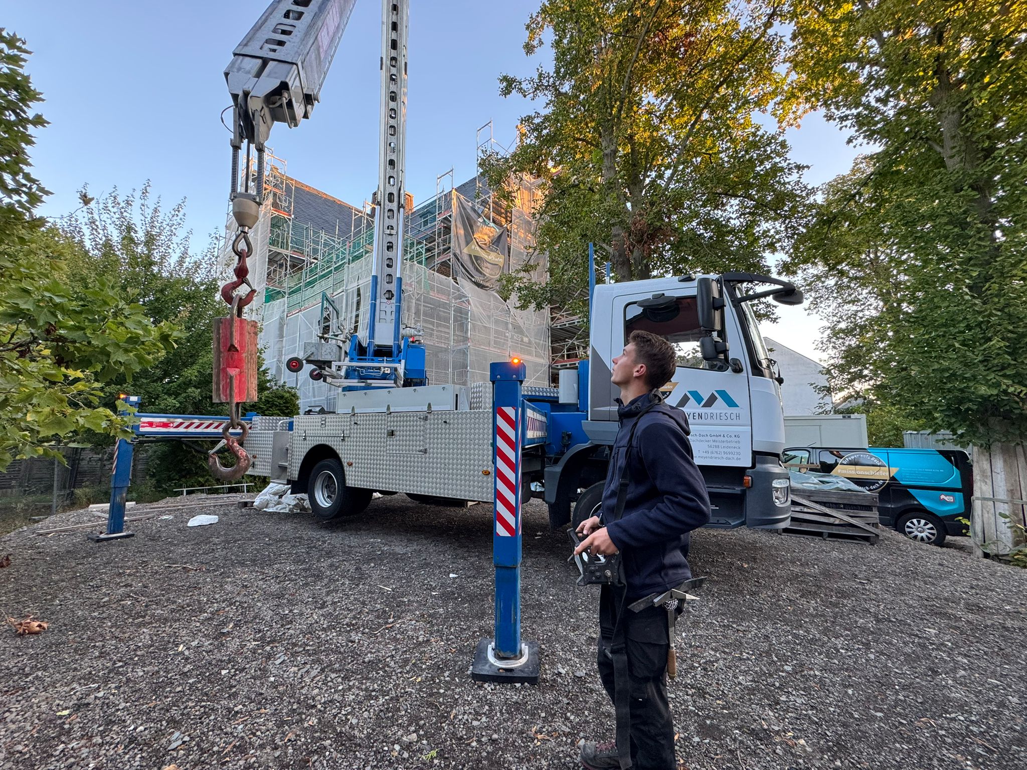 Mitarbeiter von Meyendriesch-Dach steuert eine Drohne zur Inspektion einer Kirchendach-Sanierung – Firmenfahrzeug und eingerüstetes Gebäude im Hintergrund