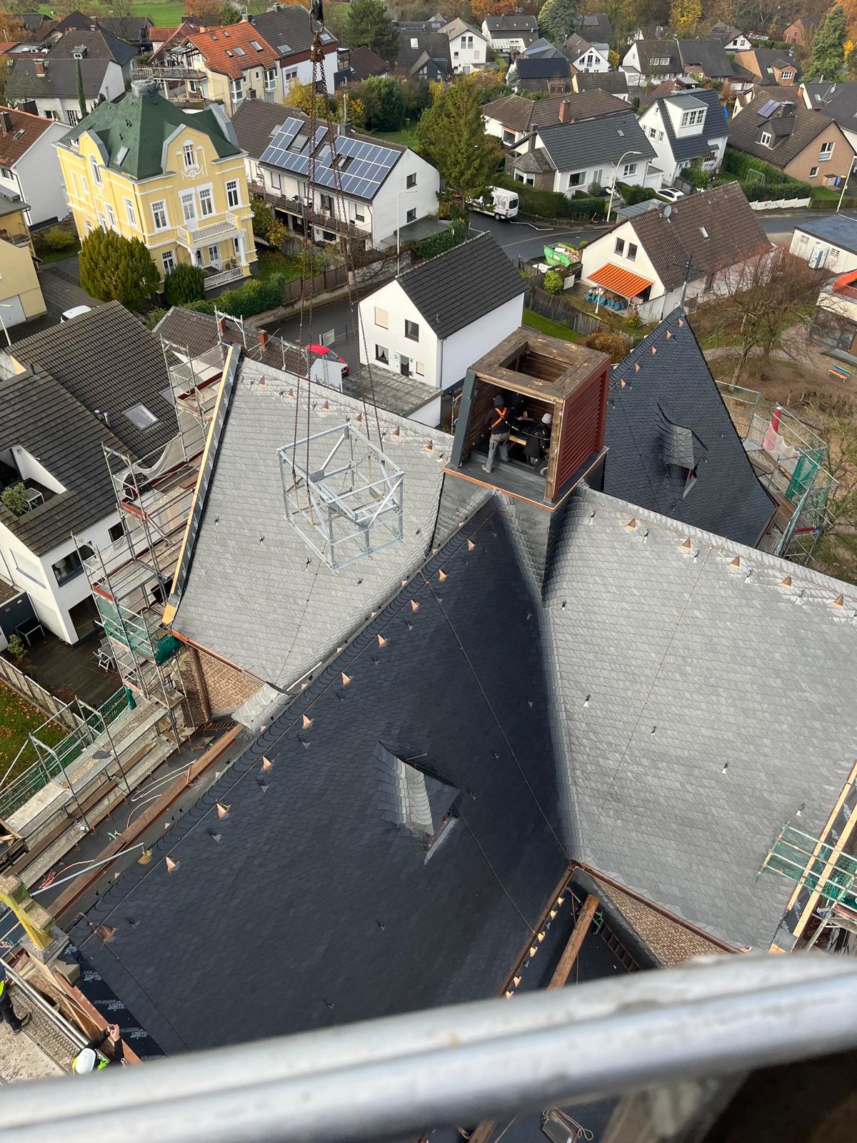 Draufsicht vom Kirchturm auf ein frisch eingedecktes Schieferdach mit Kupferdetails und laufenden Restarbeiten – Dachsanierung durch Meyendriesch-Dach mit Blick über eine Ortschaft