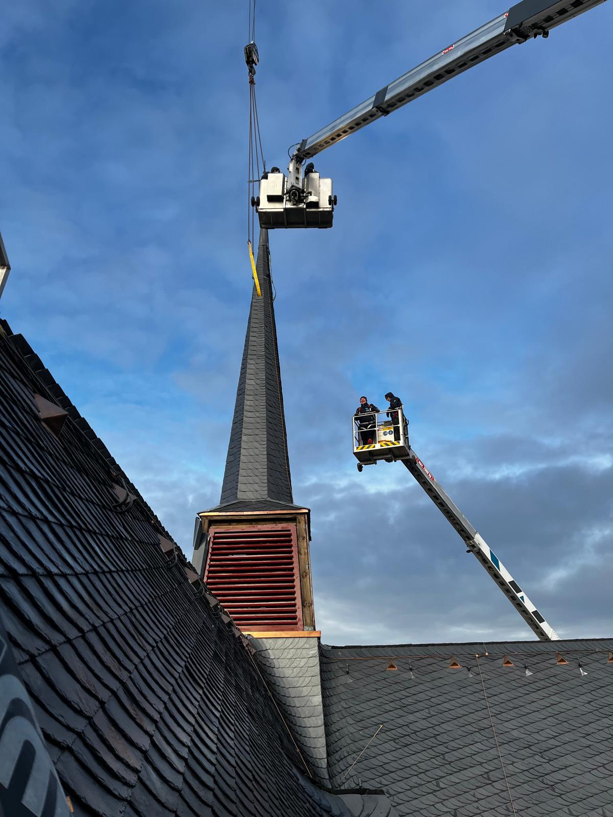 Mitarbeiter von Meyendriesch-Dach bei Schieferarbeiten an einem spitzen Kirchturm – Einsatz mit Hebebühne und Kran an einem frisch sanierten Schieferdach