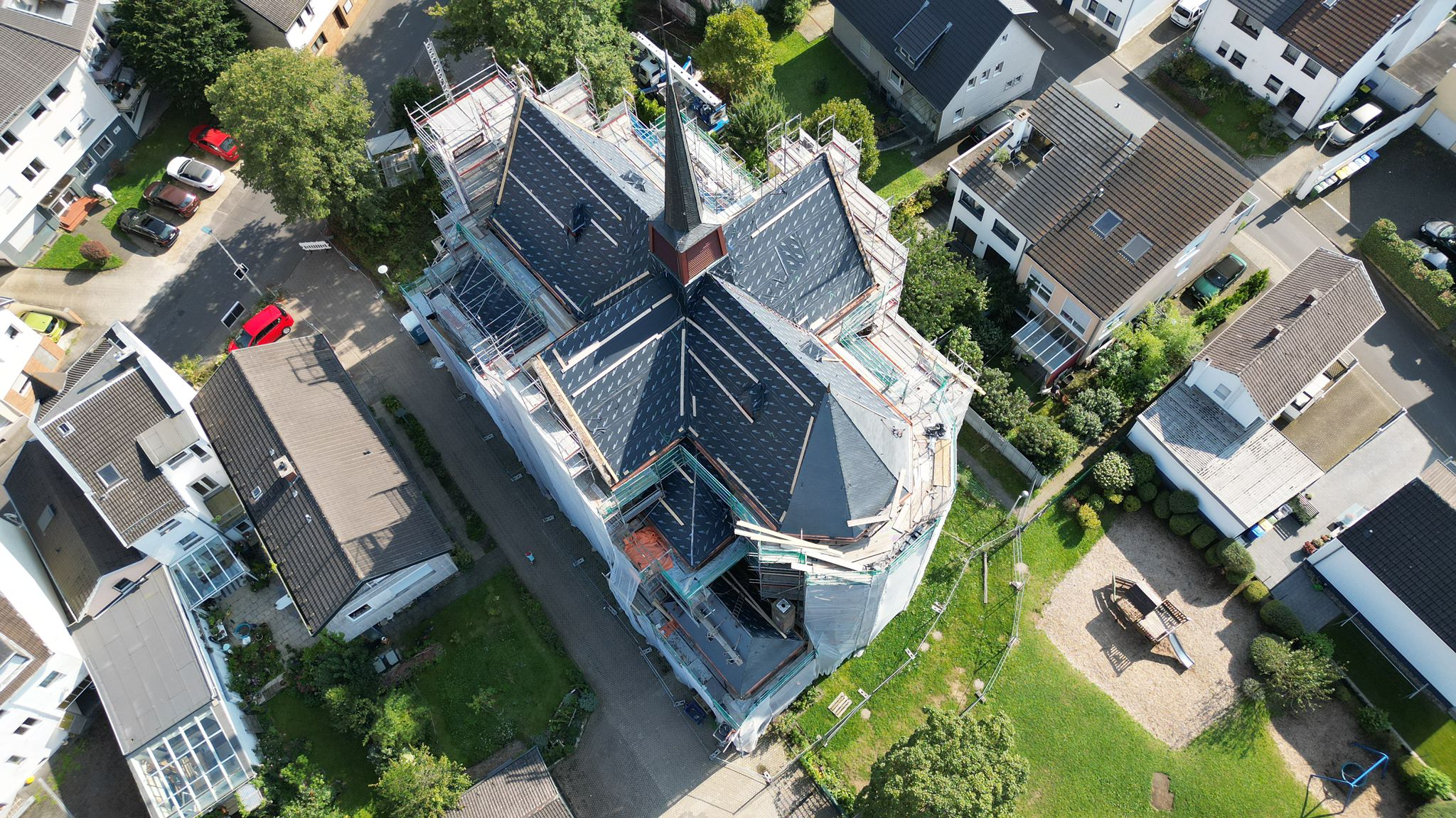 Drohnen-Luftaufnahme einer laufenden Kirchendach-Sanierung mit Schiefereindeckung und umlaufendem Gerüst – Großprojekt von Meyendriesch-Dach, Hunsrück
