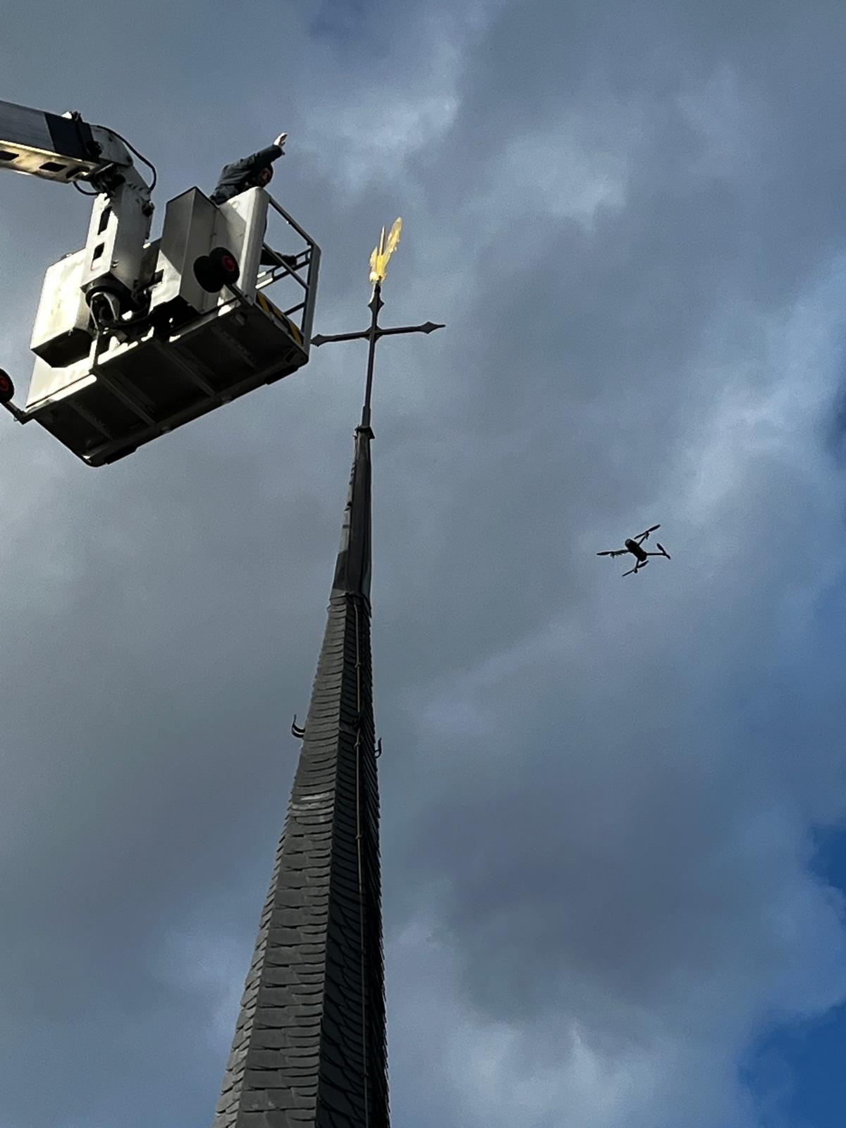 Mitarbeiter von Meyendriesch-Dach montiert per Hebebühne eine goldene Wetterfahne auf einem frisch sanierten Schieferkirchturm – begleitet von Drohnenbefliegung zur Dokumentation